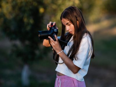 Teen girl focusing intently with a professional camera in a serene natural park, capturing the beauty of golden hour light